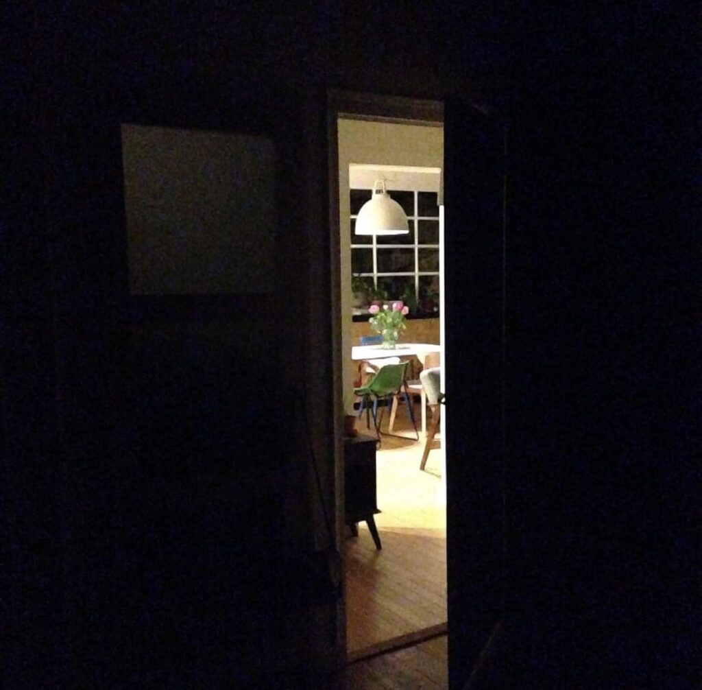 Porte entrouverte sur une pièce baignée de lumière, vue à travers l'obscurité. Image sensible d'un monde intérieur profond et intime. Un monde créatif.