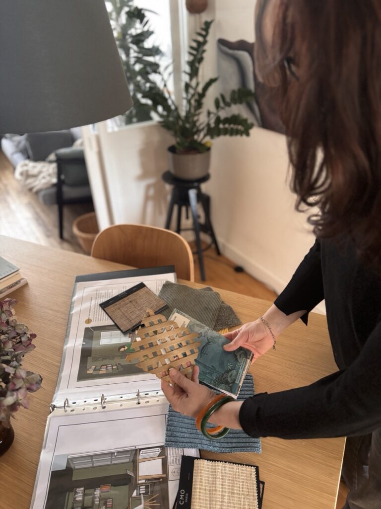 une table de travail, des matériaux, échantillons tenus par des mains et une silhouette dans la partie droite un peu floue d'une créatrice