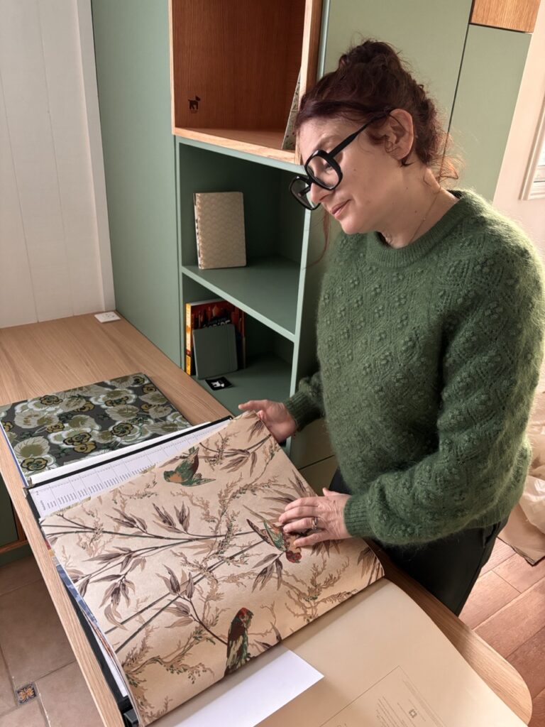 Décoratrice d'intérieur feuilletant des échantillons de papiers peints et matières dans un espace de travail, illustrant la phase de création et de composition d'un projet sur-mesure.