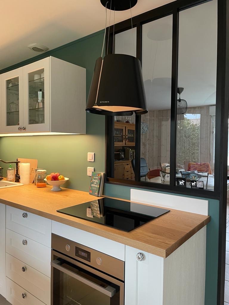 Vue de la cuisine après rénovation – plan de travail bois, mur vert et verrière noire