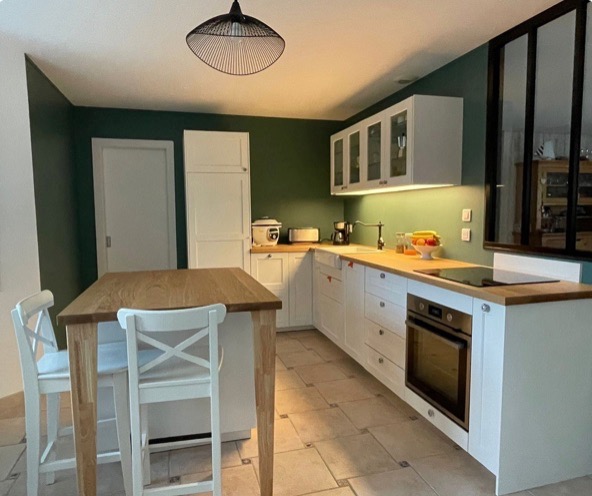 Vue générale de la cuisine rénovée à Aizenay – style cottage industriel, mur vert et bois blond