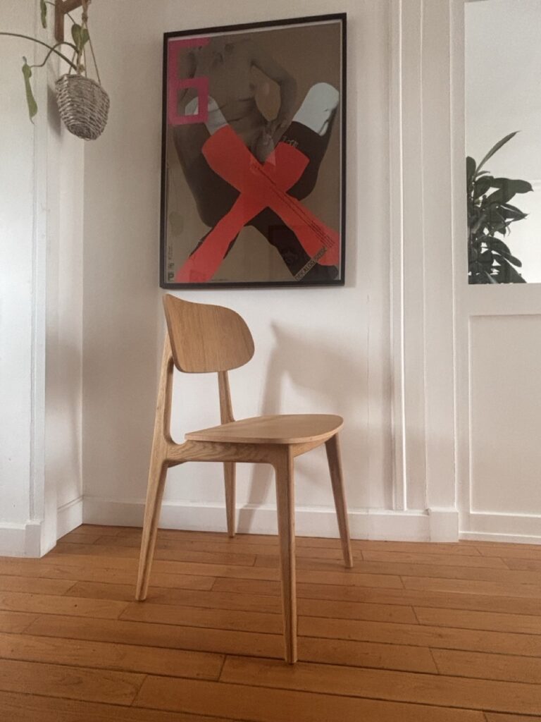 Chaise en bois devant une affiche contemporaine rouge et noire, sur parquet ancien et mur blanc.