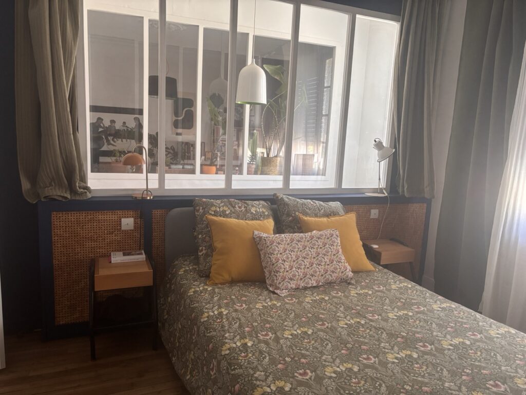 Chambre chaleureuse avec verrière intérieure, motifs floraux et matières naturelles.