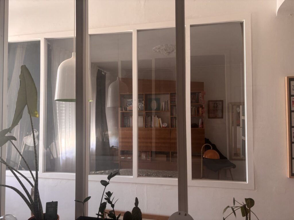 Vue intérieure à travers une verrière, avec bibliothèque vintage et plantes d'intérieur