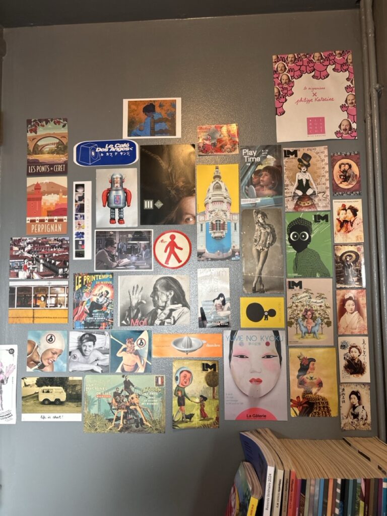 Mur recouvert de cartes postales, illustrations rétro et collages graphiques colorés.