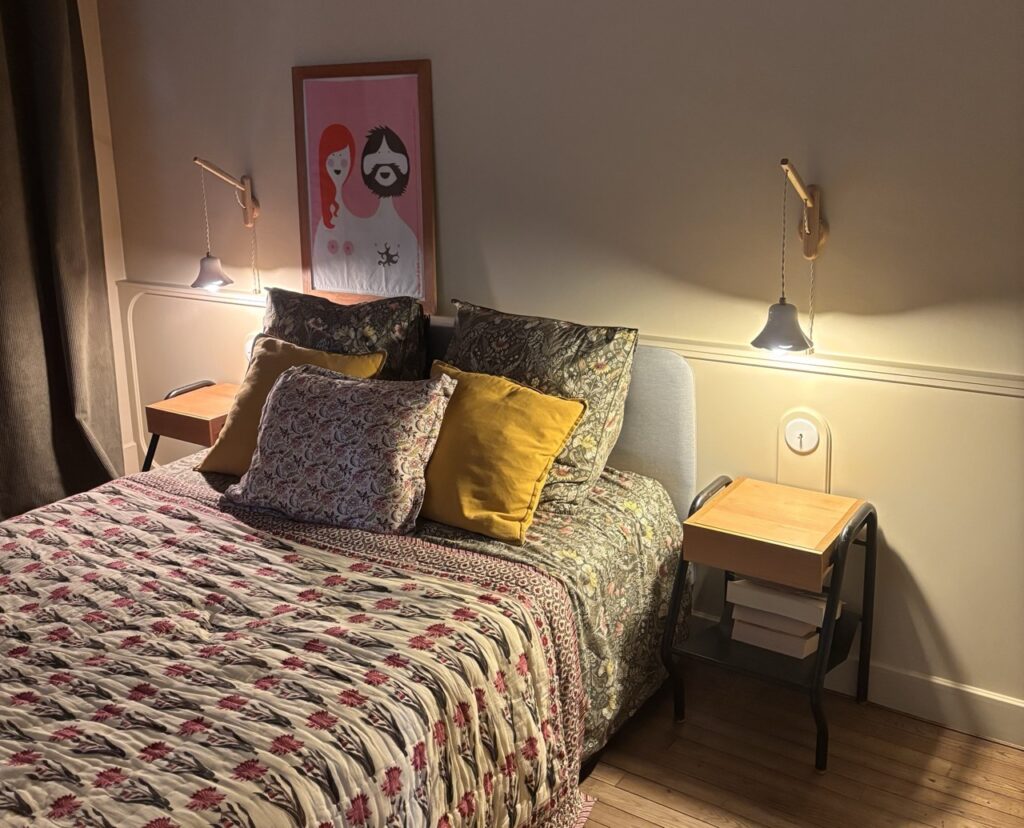 Chambre parentale avec tête de lit fleurie, coussins jaunes et liseuses en porcelaine blanche allumées