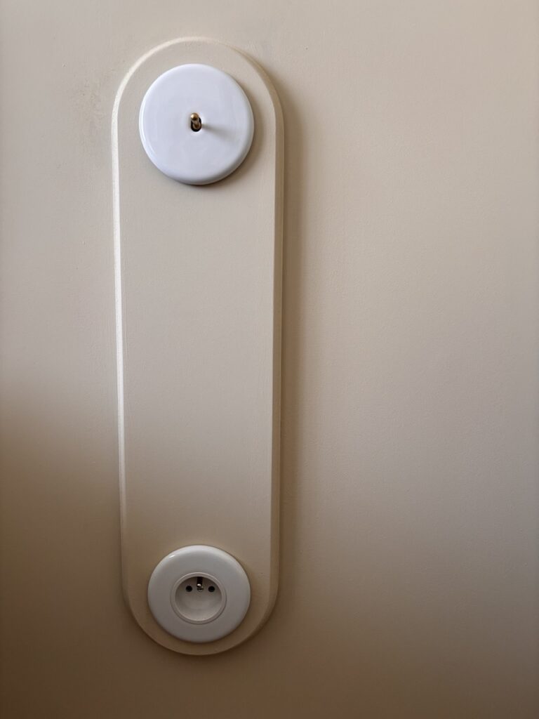 Interrupteur et prise ronds en porcelaine blanche intégrés dans un panneau mural peint ton sur ton