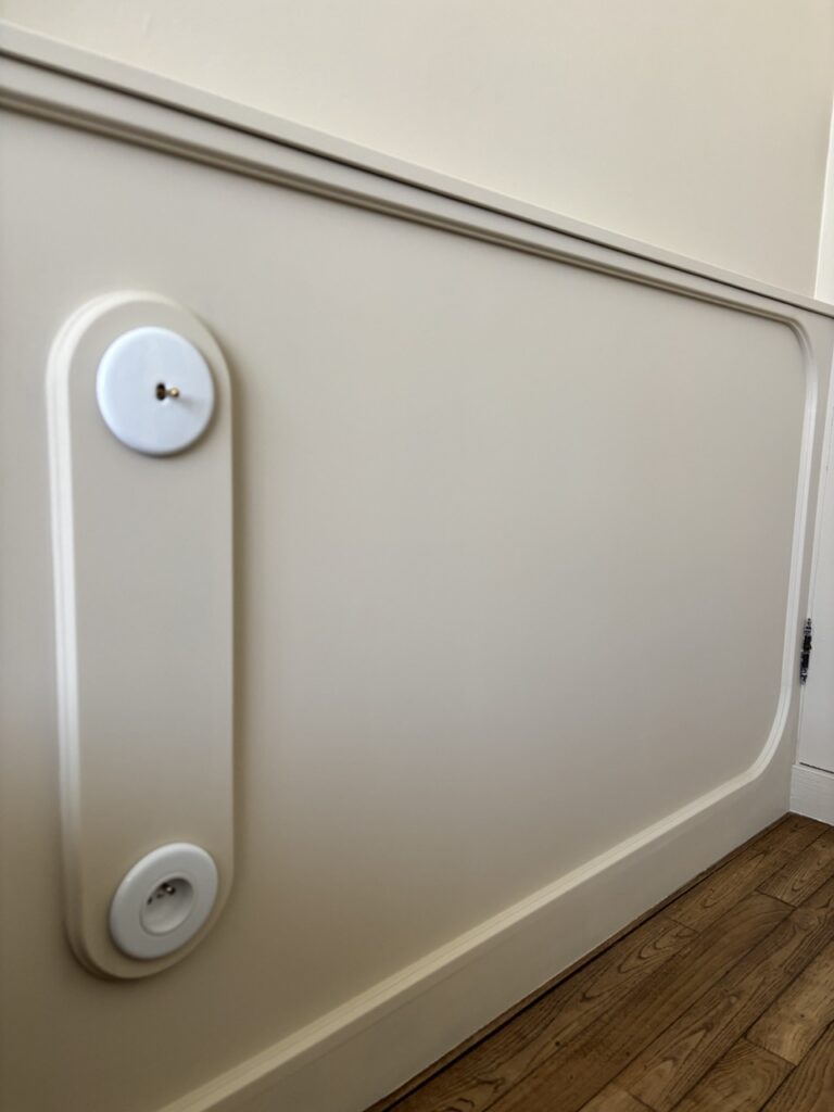 Panneau mural peint beige avec moulures arrondies et interrupteur en porcelaine blanche